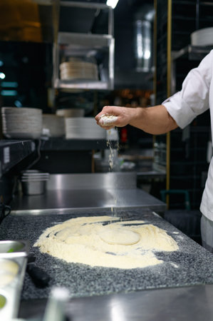 Pastry chef hands sprinkles with flour dough during kneading closeup