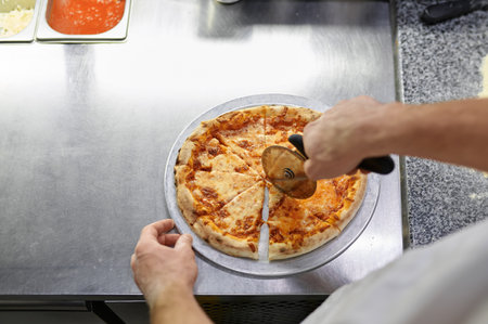Chef cutting freshly baked pizza with round knife on wooden boardの写真素材