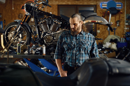 Portrait of bearded brutal biker at motorcycle in garage workshopの写真素材