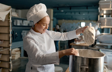 Female confectioner wearing white uniform putting flour into big metal bowlの写真素材