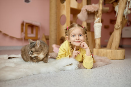Cheerful girl lying on floor with fluffy cat over animal shelter backgroundの写真素材