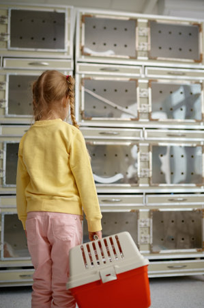Cute little girl with plastic cat carrier looking at glass pet cagesの写真素材