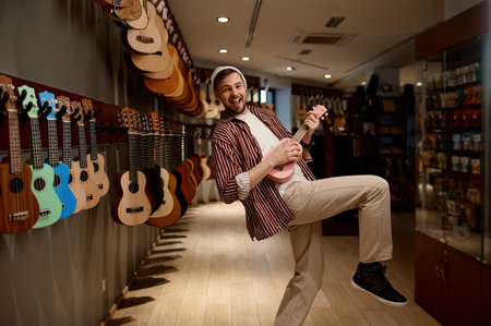 Overjoyed funny guitarist playing ukulele guitar at musical shop storeの写真素材