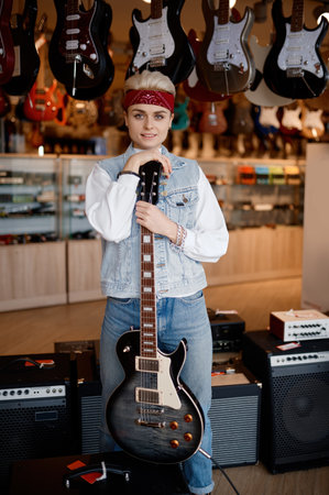 Portrait of young hipster woman musician with guitar at professional shopの写真素材