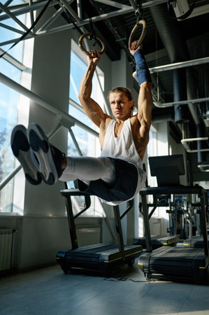 Fit male athlete training on gymnastics rings in light sport hall at gymの写真素材
