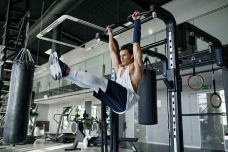 Strong energetic sportsman with perfect body pulling up on bar at sport studio