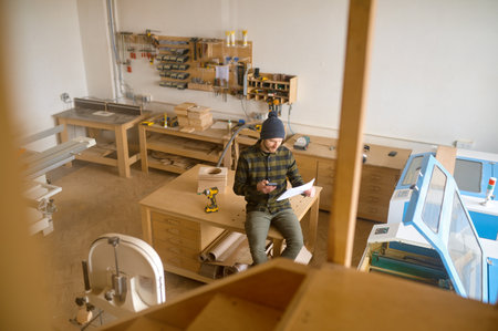 Overhead view on man carpenter sitting on table at modern joinery workshopの写真素材