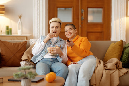 Cheerful loving lesbian woman couple eating popcorn watching movie on tvの写真素材