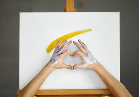 Composition of artist hands making heart shape sign over picture canvasの写真素材