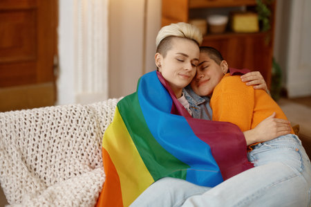 Young freedom lesbian woman cuddling in lgbt rainbow flag while sitting on sofaの写真素材