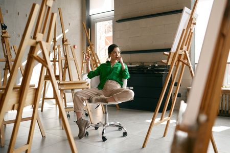 Female artist with paintbrush in hand looking seriously on her own pictureの写真素材