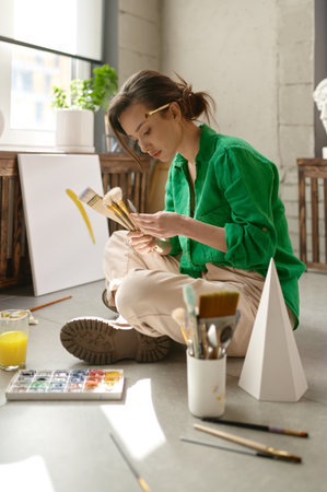 Young female artist drawing picture sitting on floor in her own art studio
