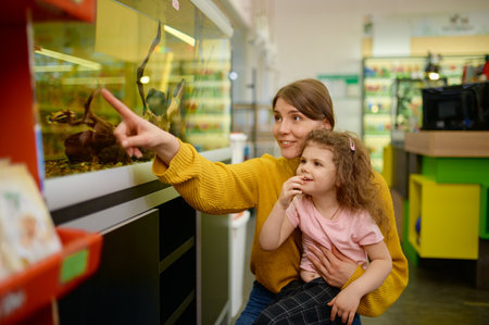 Excited mother and daughter looking on swimming fish in aquarium at pet shopの写真素材