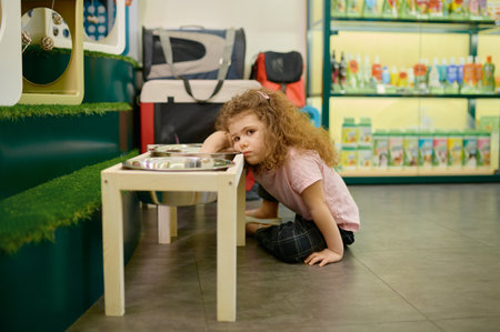 Sad little girl sitting nearby big feed bowl dreaming about dog at pet shop