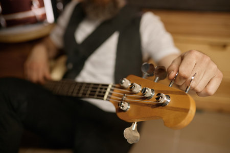 Bearded brutal guitarist tuning his musical instrument while sitting on floorの写真素材