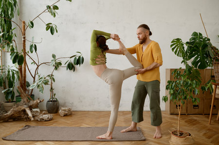 Young woman training yoga with male instructor indoors