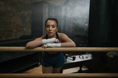 Pretty young woman boxer resting at ring ready for workoutの写真素材