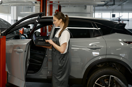 Woman auto mechanic checking customer car using laptop for diagnosticsの写真素材