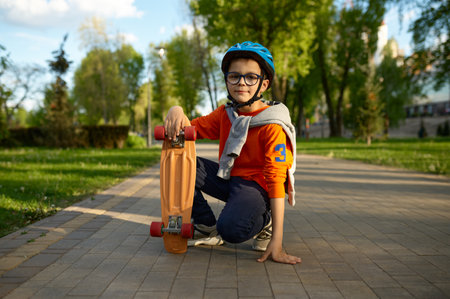 Little schoolboy wearing protective helmet sitting on asphalt with skateboardの写真素材