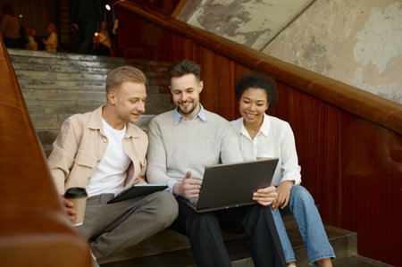 Team of coworkers using digital gadget sitting on stairs in office