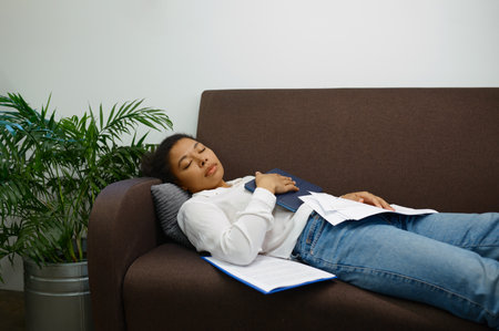Tired woman worker sleeping on sofa in corporate officeの写真素材