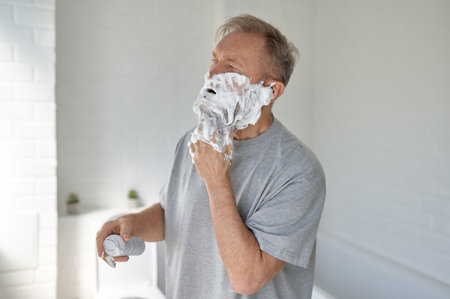 Senior man shaving face enjoying daily routine in home bathroomの写真素材
