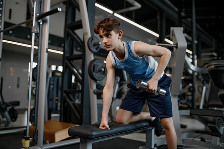 Concentrated teenager boy training arm and shoulders muscles with dumbbellsの写真素材