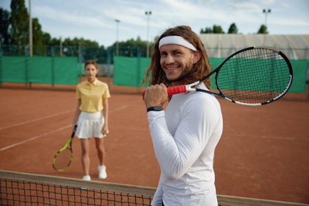 Couple of friends playing tennis on court with focus on confident manの写真素材