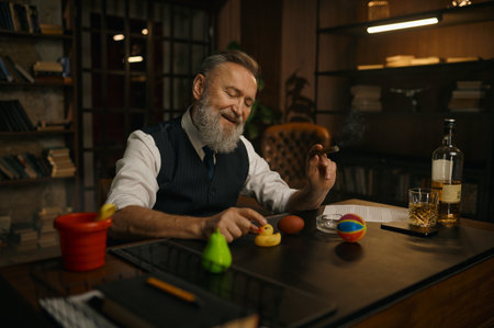 Funny elegant older businessman smoking cigar and playing toys at work tableの写真素材
