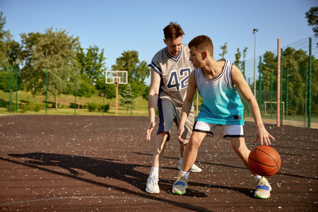 Young trainer teaching teenage boy playing basketball on street courtの写真素材
