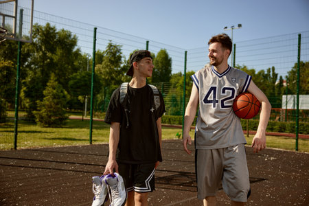Trainer and teenager boy talking after practicing basketball on street court