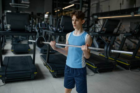 Strong teenager boy lifting barbell at modern gym enjoying sports trainingの写真素材