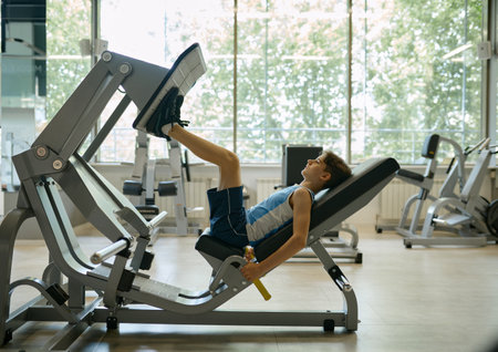 Preteen boy training legs on sports equipment at gym