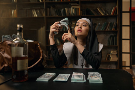 Pretty confident woman in nun dress sitting at table with money stacksの写真素材