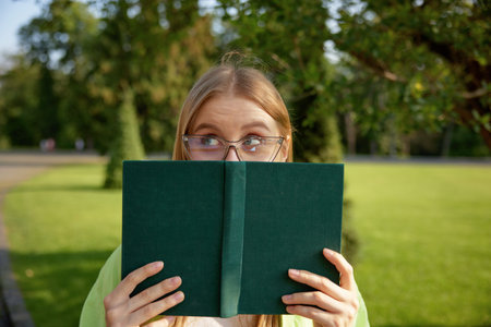 Portrait of cute funny female student hiding behind book