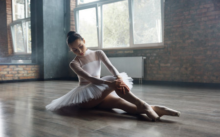 Young ballet dancer girl posing at studio sitting on floorの写真素材