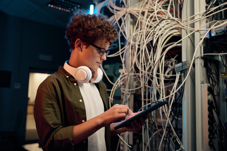 Serious young IT man working in data center standing at open server rack cabinetの写真素材