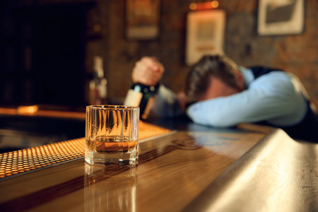 Drunk man sleeping at bar counter with focus on alcoholic drink in glassの写真素材