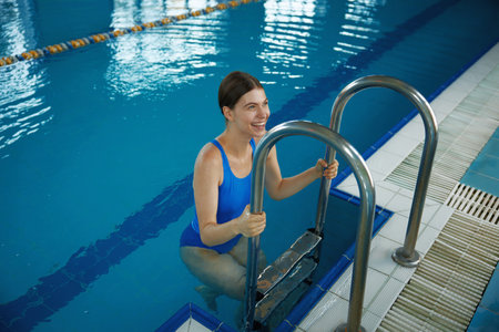 Happy smiling woman climbing out by steps of swimming pool