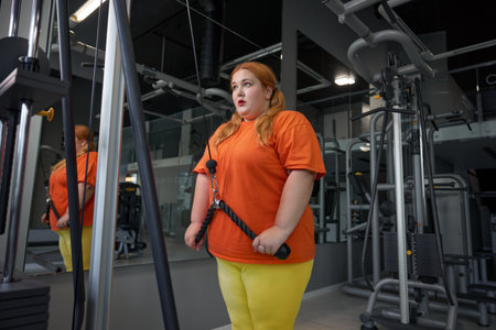Exhausted excess overweight woman training with equipment at gym