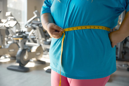 Closeup waistline of overweight woman wrapped in measuring tapeの写真素材