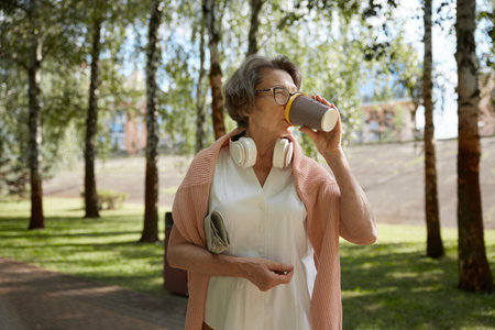 Happy retired woman with coffee walking through city park