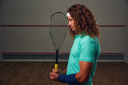 Young pensive racketball player with racket standing backsideの写真素材