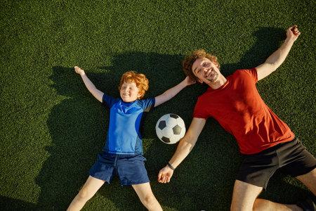 Overjoyed father and little son child lying on soccer field grassの写真素材