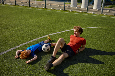 Tired father and son soccer player lying on grass of football fieldの写真素材