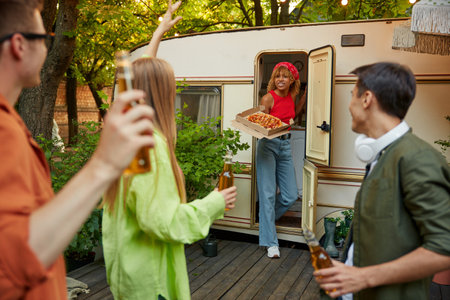 Friends camping party at trailer concept, young girl serving table with pizzaの写真素材