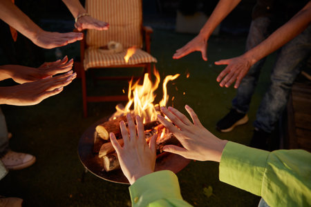 Group of young people warming hands over burning campfire closeup
