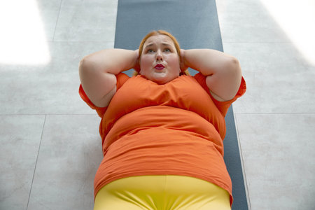 Overweight woman doing abs crunch lying on mat while training at gym