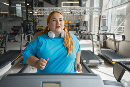 Active obese woman running on treadmill track enjoying cardio exerciseの写真素材