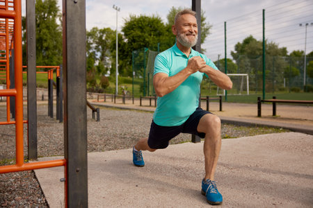 Senior man doing lunges physical exercises at sport field outdoorsの写真素材